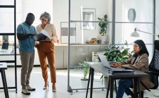 Customize Solution Mature businesswoman and African American male employee discussing document while standing in the center of modern coworking area